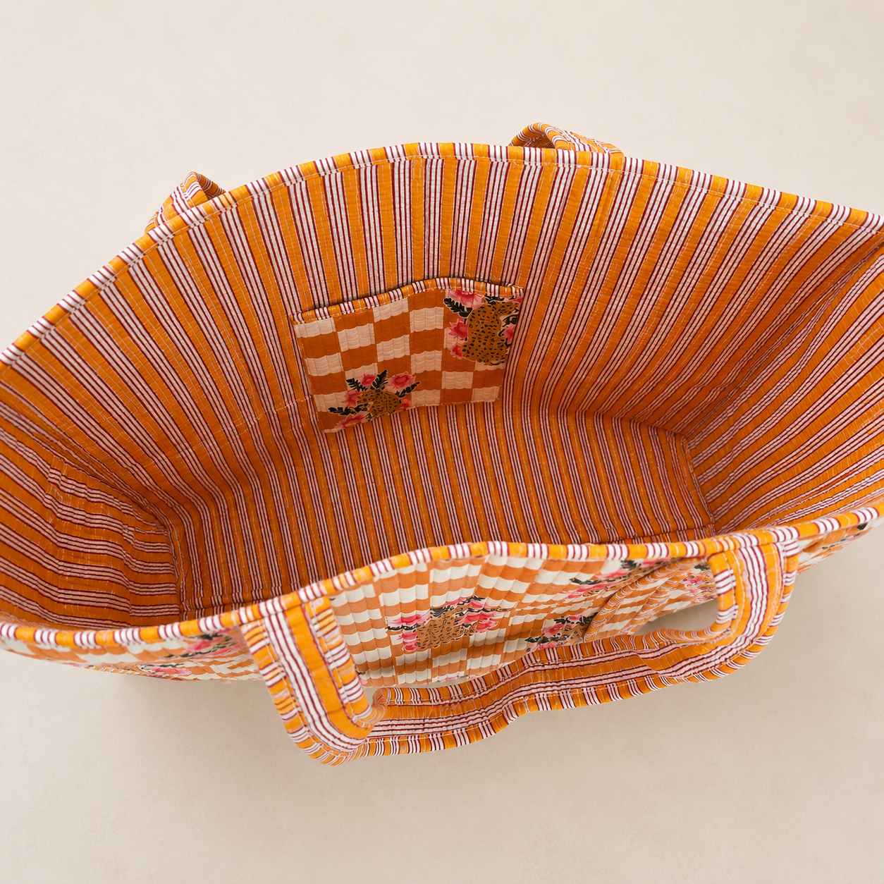Binnenkant van een ruime katoenen totebag met oranje gestreepte voering en binnenvak met luipaard- en bloemenprint.