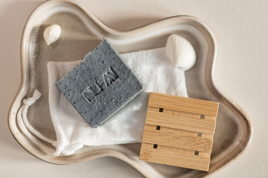 Exfoliërende NU-MI scrubzeep voor vette en onzuivere huid op een doek met houten zeepplank in keramische schaal.