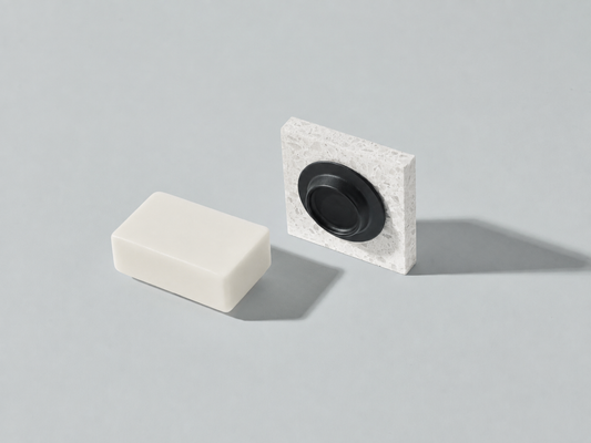 Zwarte Soapi magnetische zeephouder met een natuurlijke zeepbar op een lichte stenen ondergrond