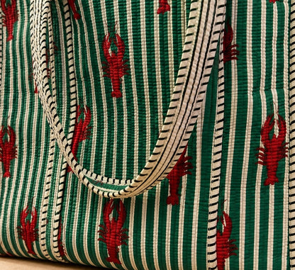 Close-up van een gewatteerde totebag met groene en witte strepen, rode kreeftenprint en stevige gestreepte hengsels.