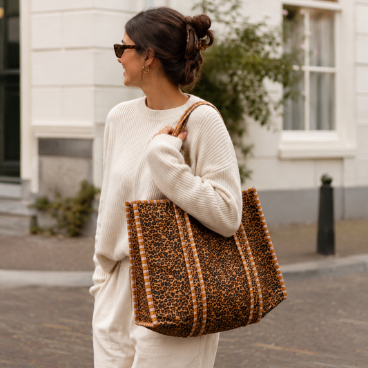 Vrouw draagt een grote NU-MÍ tote bag met luipaardprint in een Nederlandse stadsomgeving.