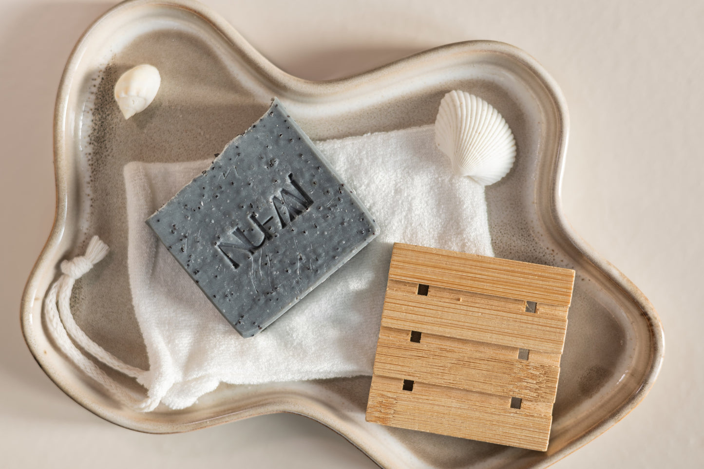 Exfoliërende NU-MI scrubzeep voor vette en onzuivere huid op een doek met houten zeepplank in keramische schaal.