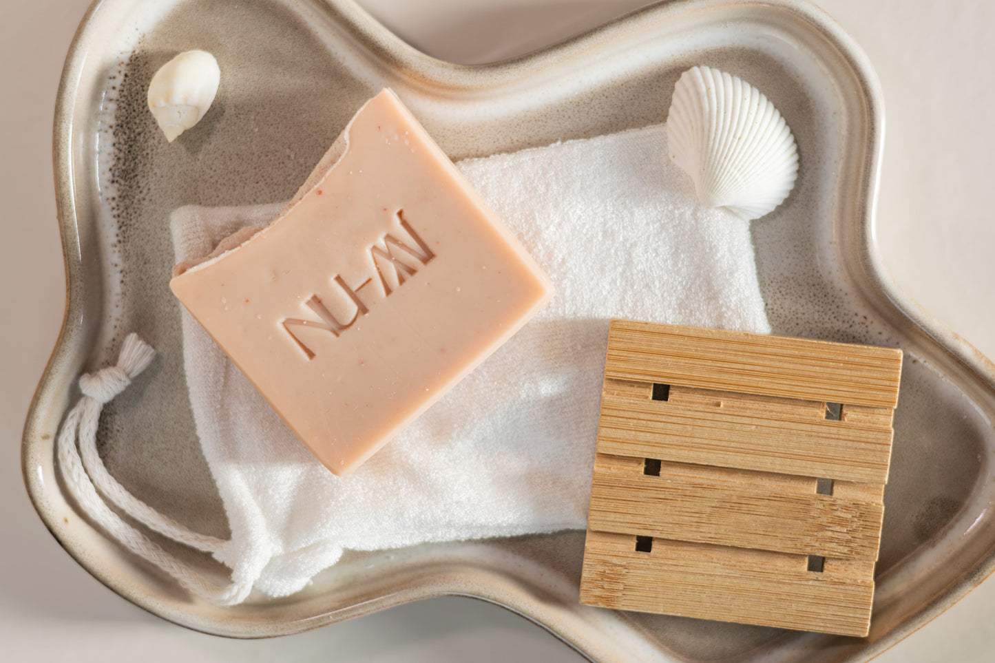 NU-MI roze zeep voor gevoelige huid op een zachte doek met houten zeepplank in keramische schaal.