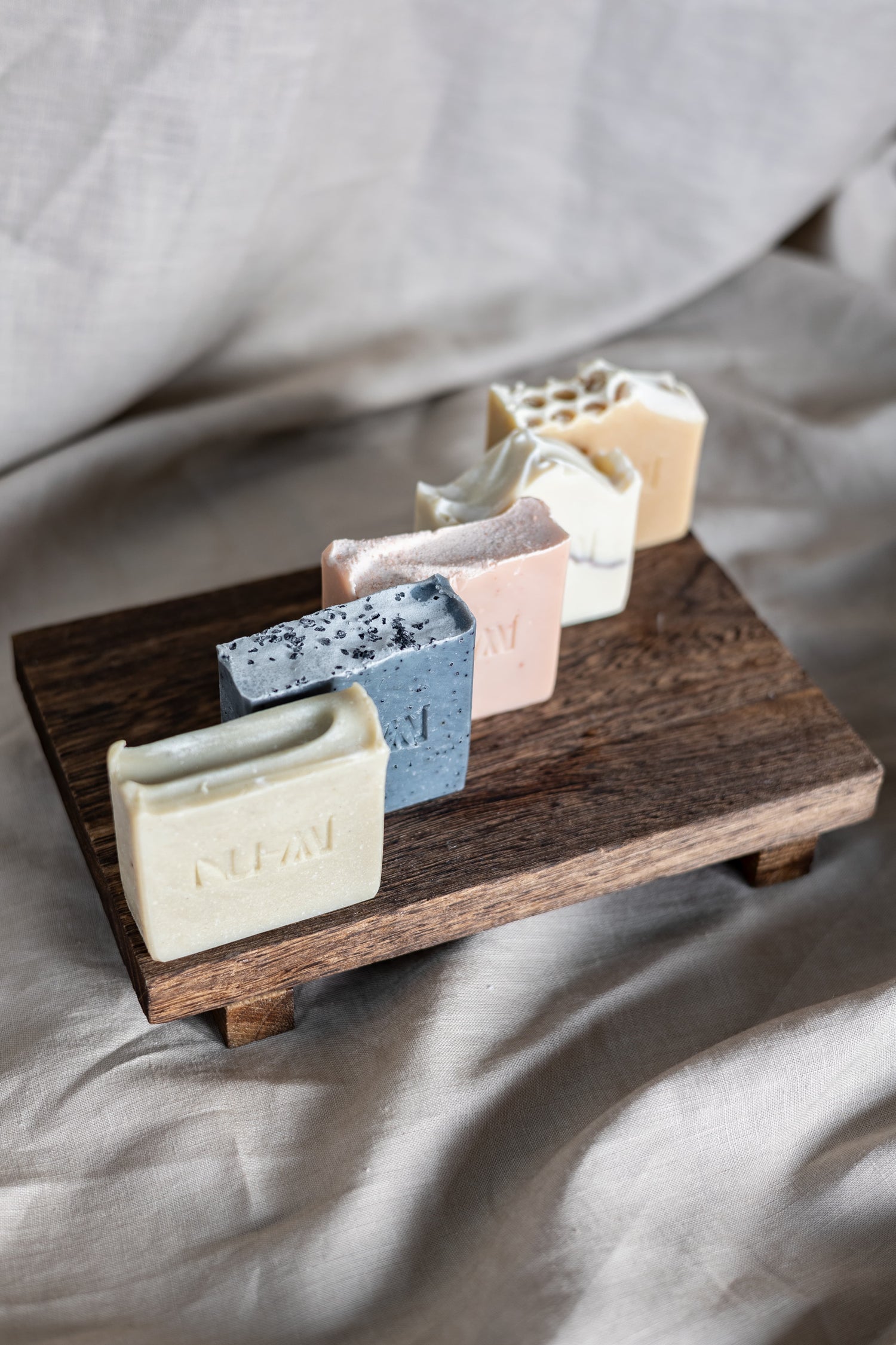 NU-MI handgemaakte zeepbars in verschillende varianten op een houten display.
